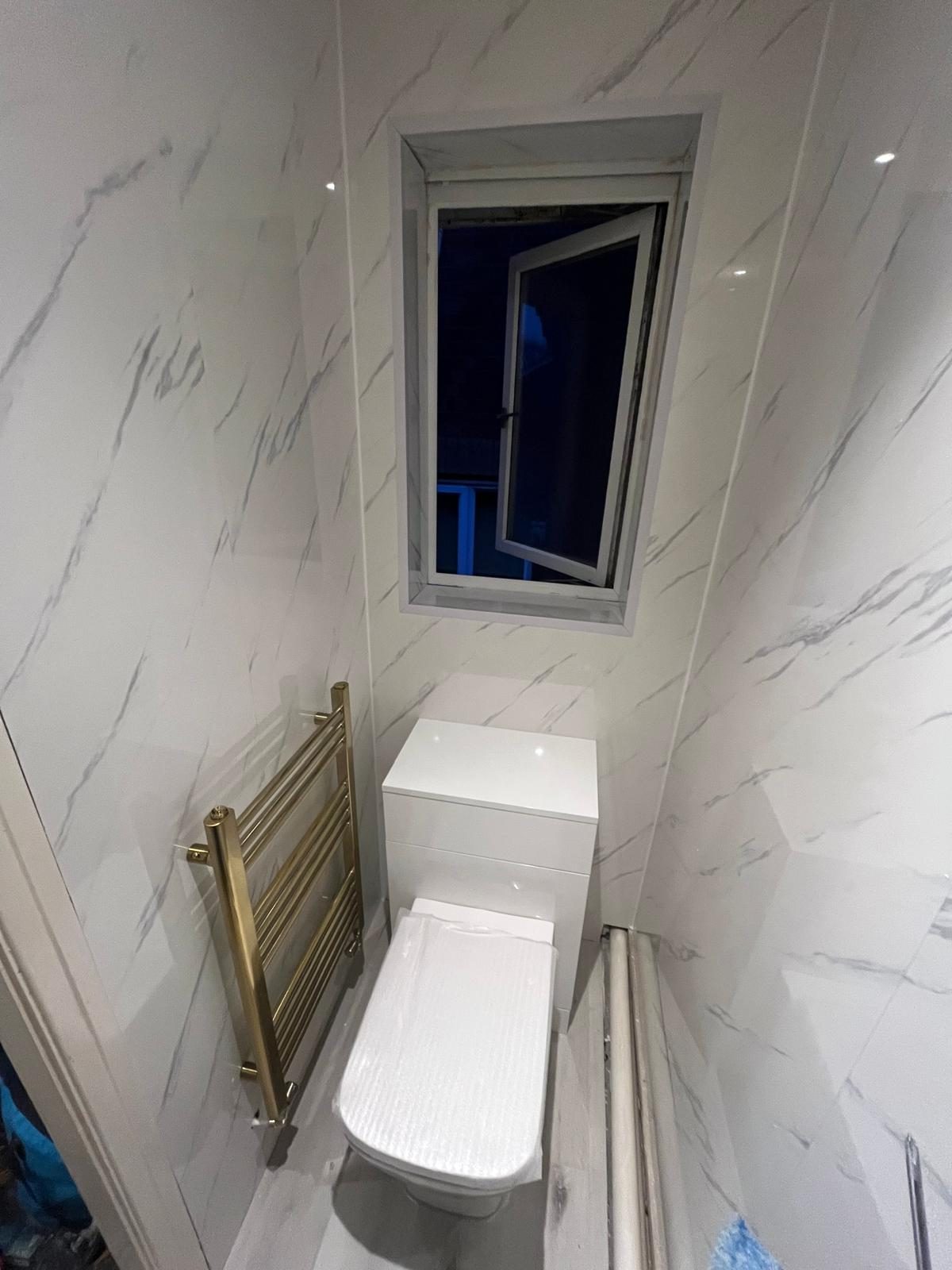 Finished cloakroom WC with marble-effect wall panels and brushed gold towel rail