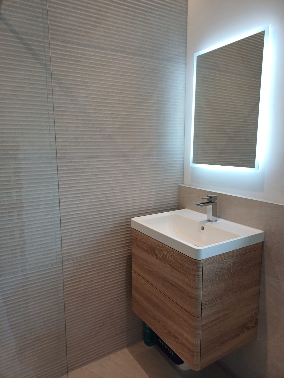 Wall-hung wood-effect vanity unit with basin and illuminated LED mirror after a bathroom renovation