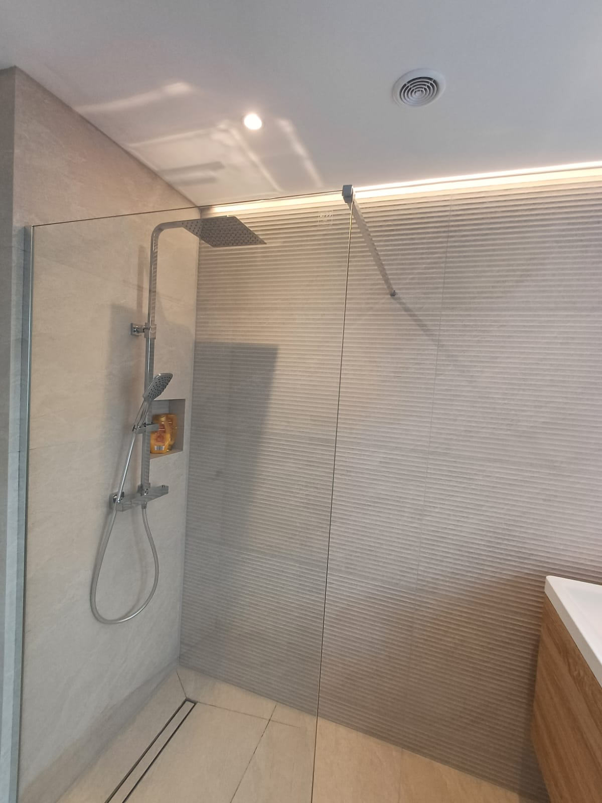 Wet room style walk-in shower with linear drain, glass screen and chrome rainfall shower set