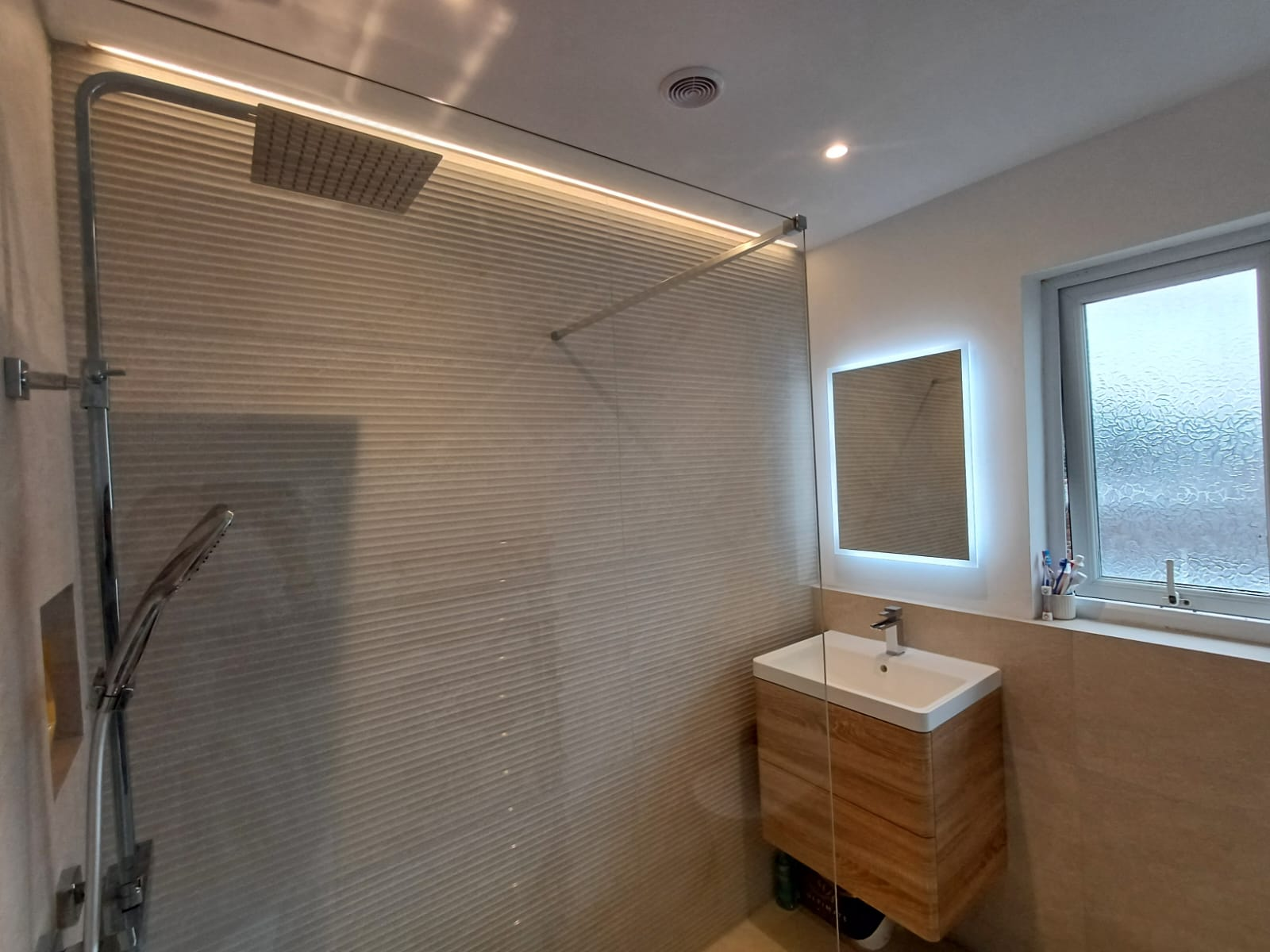 Walk-in shower installation with glass screen, chrome rainfall shower and wall-hung vanity basin