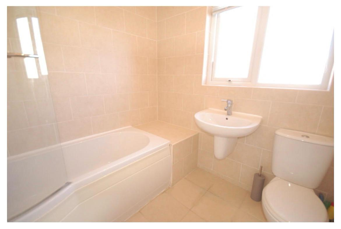 Dated beige tiled bathroom with bath, pedestal basin and toilet before refurbishment