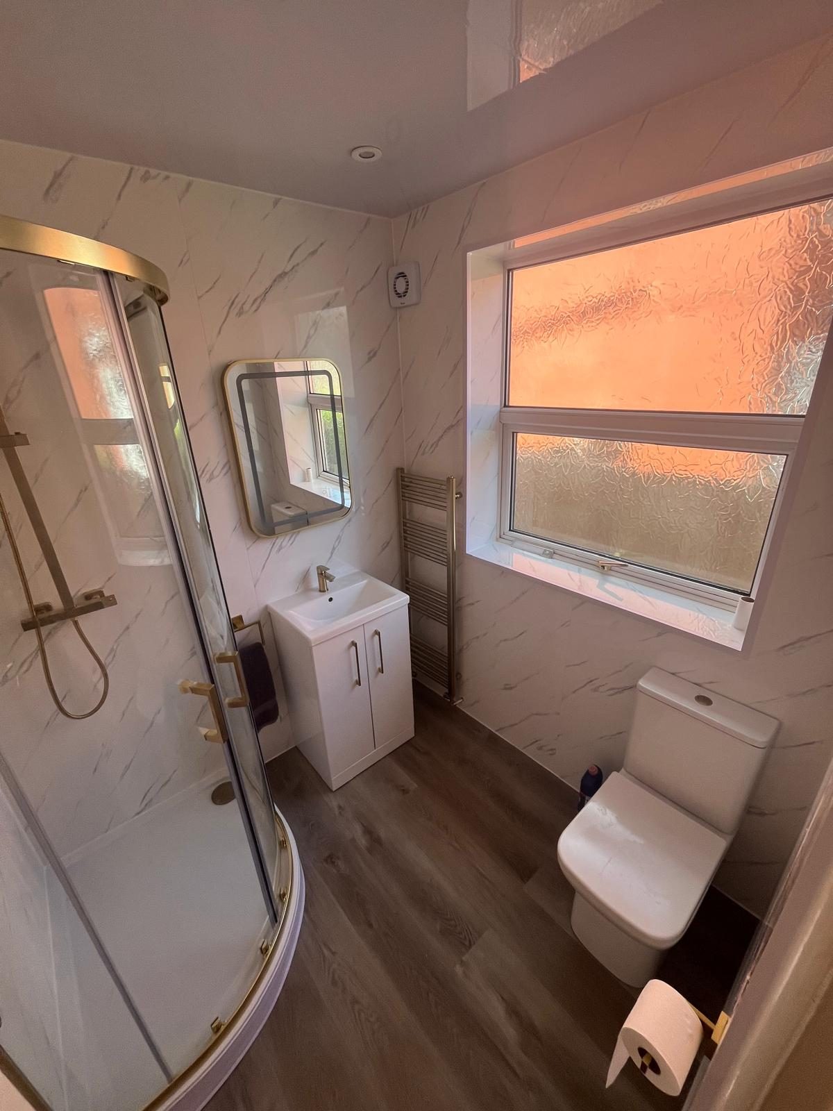 Completed bathroom renovation with quadrant shower enclosure, vanity unit and wood-effect flooring